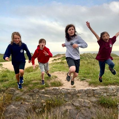 Children from Blue Horizons adaptive surf club wearing Blue Horizons hoodies running and jumping on coastal dunes in Pembrokeshire.