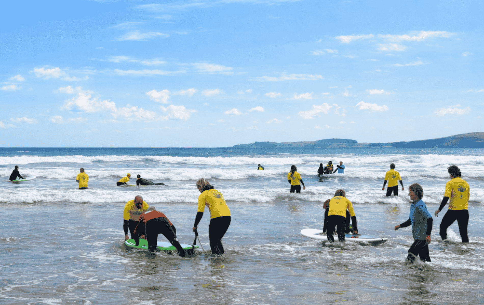 Volunteers in yellow Blue Horizons tops supporting adaptive surfers during an inclusive surf session on the Pembrokeshire coast.