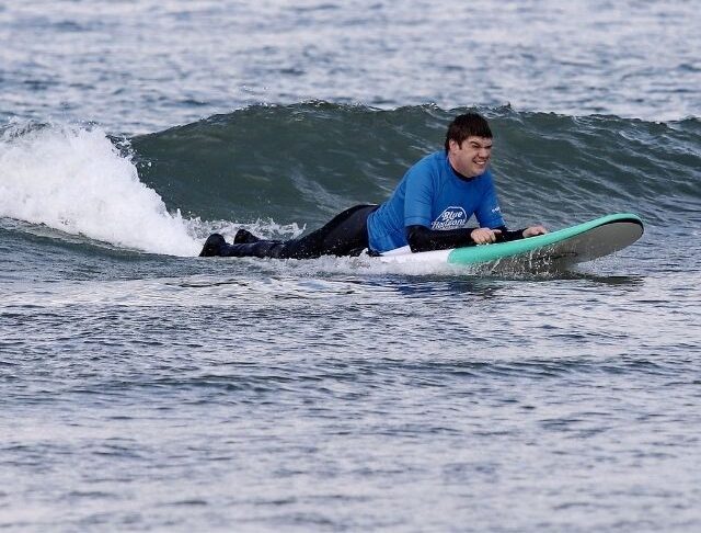 Adaptive surfer riding a small wave during a Blue Horizons inclusive surf session in Pembrokeshire.