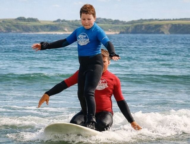 Child learning to surf during an adaptive surf lesson with Blue Horizons in Pembrokeshire, supported by an instructor in shallow water.