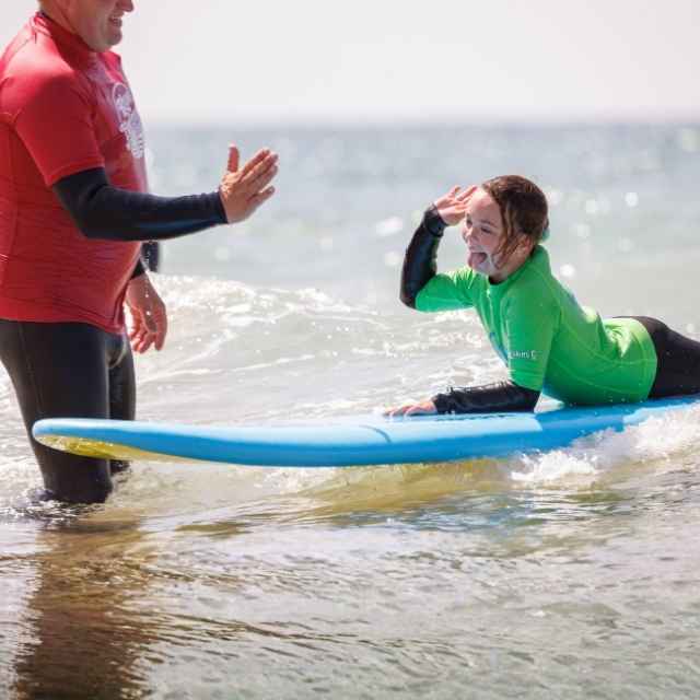 Blue Horizons instructor helping a young surfer during a community kids club surfing lesson in Pembrokeshire.