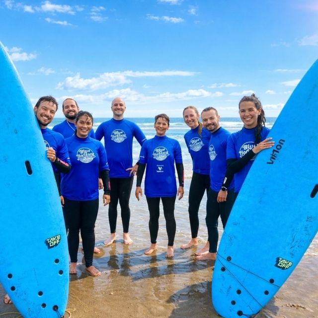 Adaptive surf instructors and volunteers from Blue Horizons standing on the beach in Pembrokeshire wearing blue surf tops and holding surfboards.