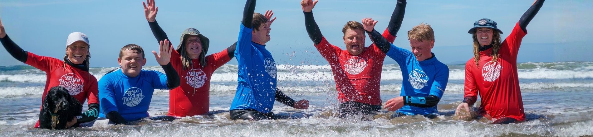 Group of adaptive surfers and instructors from Blue Horizons celebrating in the sea after an inclusive surfing session in Pembrokeshire