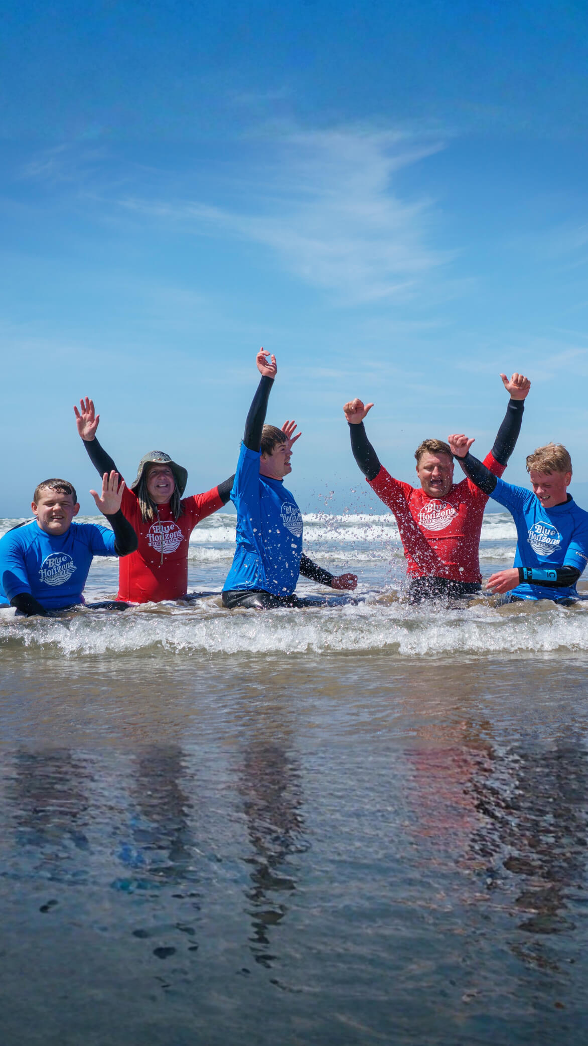 Group of adaptive surfers and instructors from Blue Horizons celebrating in the sea after an inclusive surfing session in Pembrokeshire.