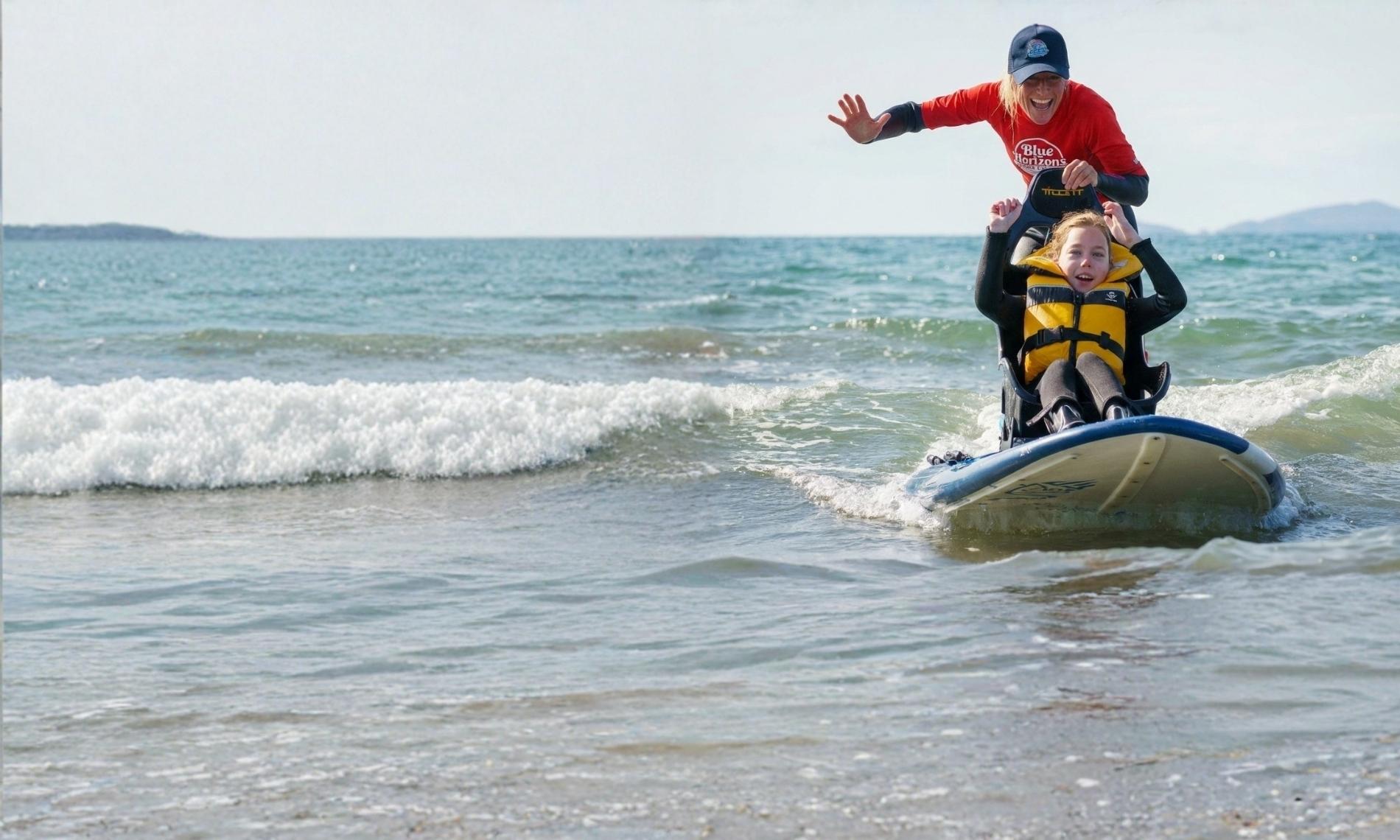 Adaptive surf instructor guiding a child on a seated surfboard during an inclusive surfing lesson with Blue Horizons on the Pembrokeshire coast