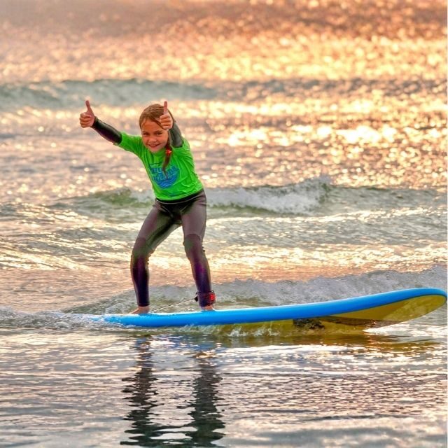 Child surfing with thumbs up during a Blue Horizons kids surf club session in Pembrokeshire.